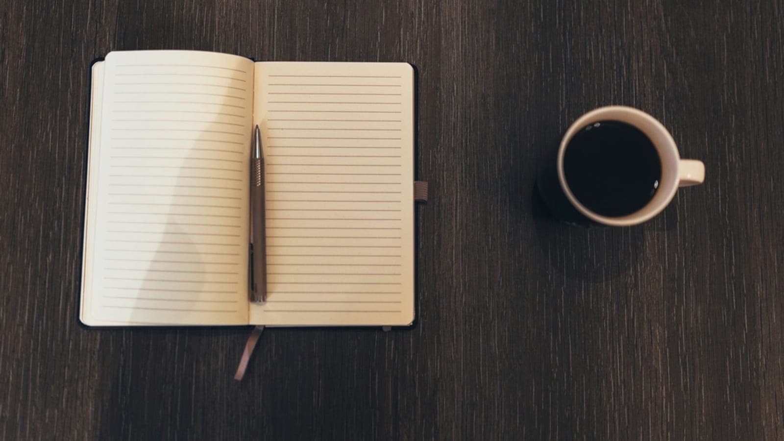 An open journal with a pen and a cup of coffee