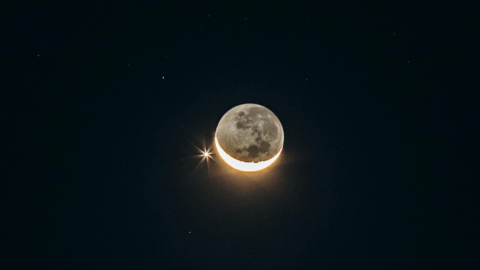 A crescent moon and a bright star in the night sky